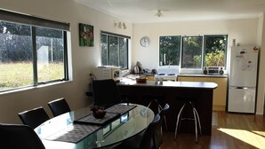Cozinha moderna com mesa de jantar de vidro, cadeiras pretas e vista para o exterior através de grandes janelas.