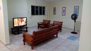 A living room with a TV, wooden furniture, a standing fan, and framed pictures on the wall. - 1st floor house in Olinda, whitewashed house, 100 meters from the beach. (Casa Caiada)
