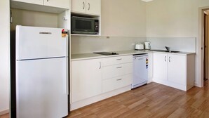 Une cuisine de taille réduite équipée d’un réfrigérateur, d’un four à micro-ondes, d’un lave-vaisselle et de meubles de rangement blancs.