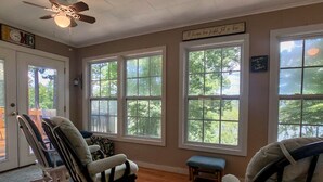 Une pièce dotée de grandes fenêtres, d’un ventilateur de plafond et offrant une vue sur les arbres à l’extérieur.