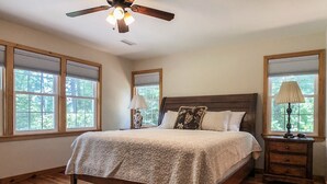 Une chambre avec un grand lit, un plancher en bois, un ventilateur de plafond et des fenêtres équipées de stores.