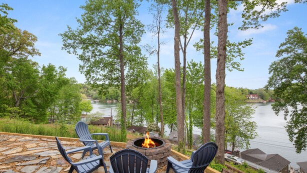 Une terrasse en pierre avec quatre chaises Adirondack et un foyer extérieur, le tout offrant une vue sur un lac.