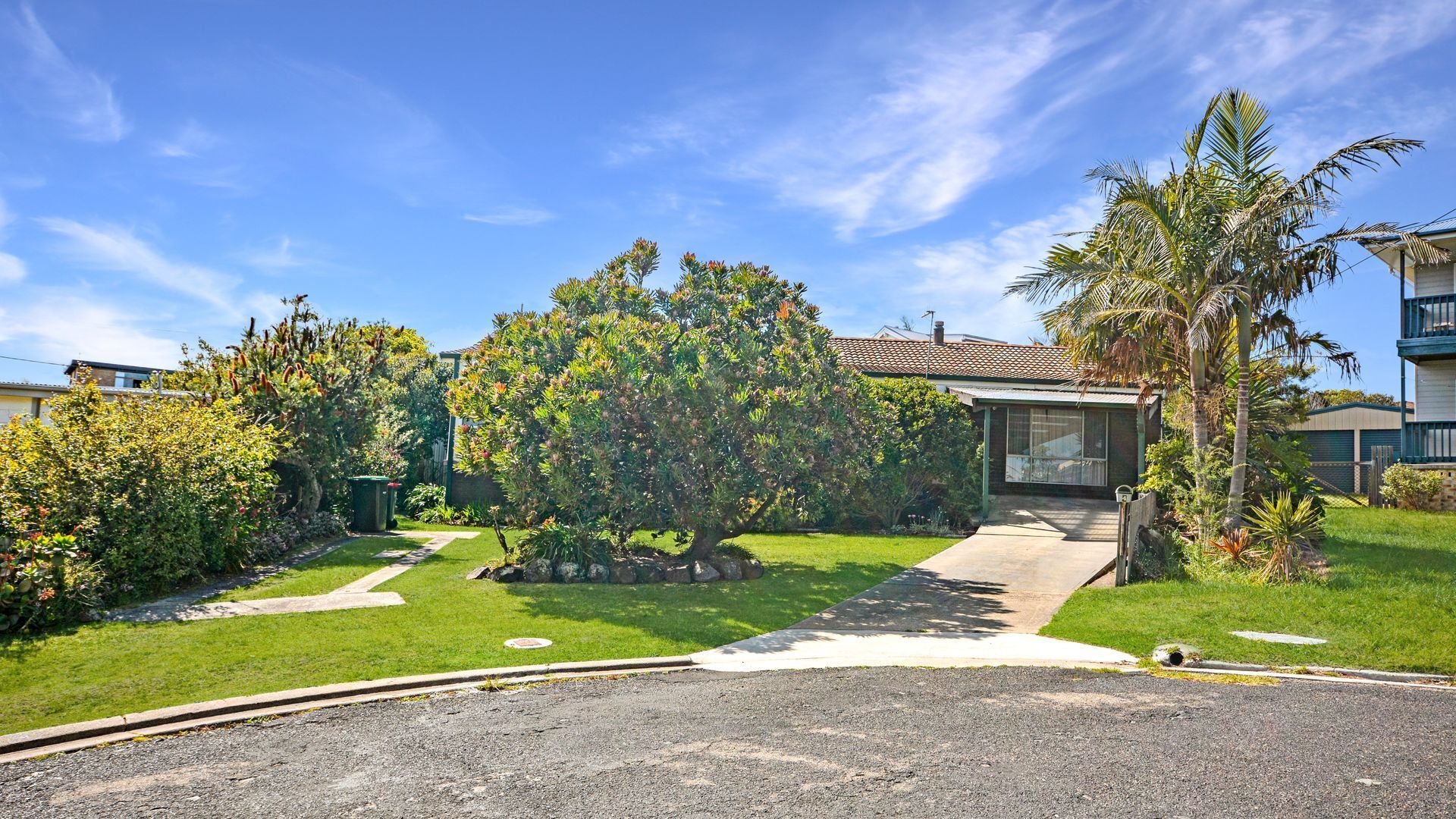 A residential property with a well-maintained lawn, a pathway leading to the house, and a variety of trees and shrubs.
