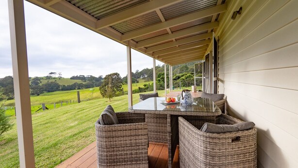 Un espacio de estar al aire libre techado con muebles de mimbre, una mesa de vidrio y una vista panorámica de un paisaje verde.