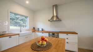 Cocina moderna con armarios blancos, encimera de madera, campana extractora de acero inoxidable y ventana con vistas a zonas verdes.