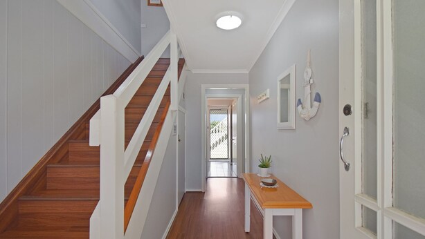 A staircase with wooden steps and white railings leading to a landing. A small table with a plant and a bowl is placed on the landing. - 158 Wallaga Lake Road (WALLAGA LAKE)