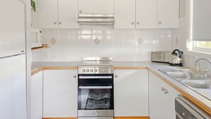 A modern kitchen with white cabinetry, a built-in oven, a stovetop, a toaster, and a kettle. - 158 Wallaga Lake Road (WALLAGA LAKE)
