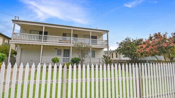 A two-story house with a balcony, a garage, and a white picket fence. - 158 Wallaga Lake Road (WALLAGA LAKE)