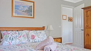 A bedroom with a wooden bed, floral bedding, a painting of a landscape, a nightstand, a lamp, and a wooden wardrobe. - 158 Wallaga Lake Road (WALLAGA LAKE)