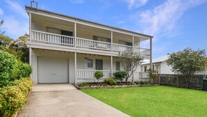 A two-story residential building with a front garage, a covered front porch, and a small front yard with a lawn and shrubs. - 158 Wallaga Lake Road (WALLAGA LAKE)