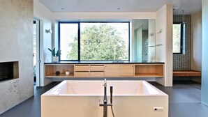 A modern bathroom with a large bathtub, a window with a view of trees, and a minimalist design. - Award-winning ocean view luxury master suite. Perfect romantic retreat (Tiburon)