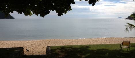 A beach with a chair and a dog, a grassy area, and a view of the sea and distant land.