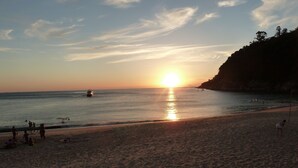 Een strand met mensen, een boot en een zonsondergang.