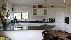 A modern kitchen with white cabinets, a large island, and a dining area with a wicker chair.