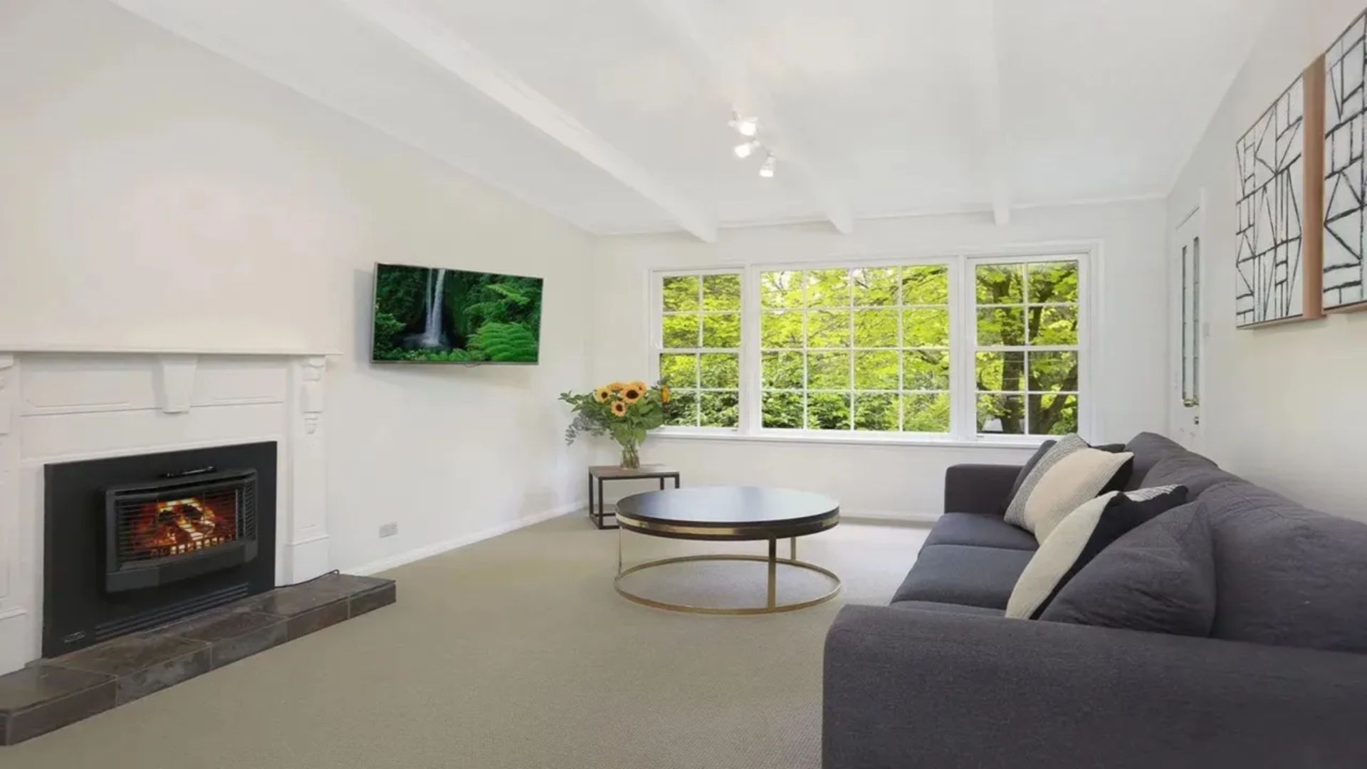 A living room with a fireplace, a sofa, a coffee table, and a large window with a view of trees.