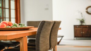 Un coin repas avec une table et des chaises en bois, un panier de fruits posé sur la table et un buffet en arrière-plan.