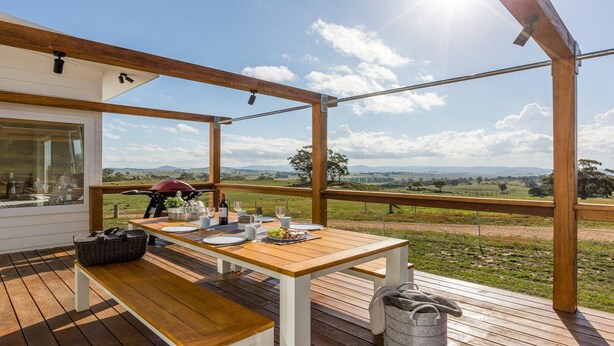 A wooden deck with a table set for dining, overlooking a grassy landscape with distant hills.