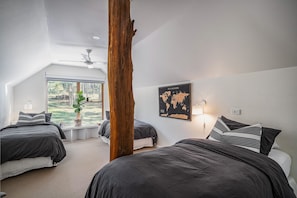 Une chambre avec deux lits, une grande fenêtre, une carte du monde accrochée au mur et une poutre en bois.