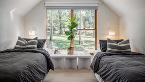 Ein Schlafzimmer mit zwei Betten, einem großen Fenster und Blick auf einen Wald.