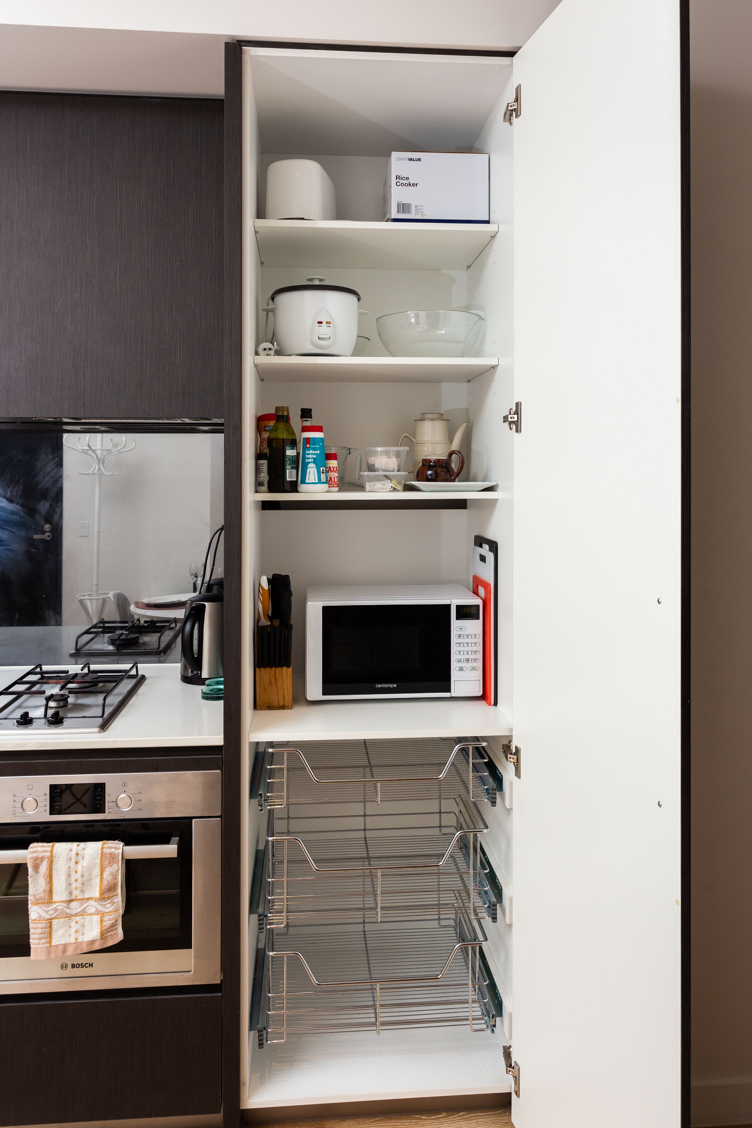 A kitchen with a Bosch oven, a microwave, and a rice cooker on the shelves.