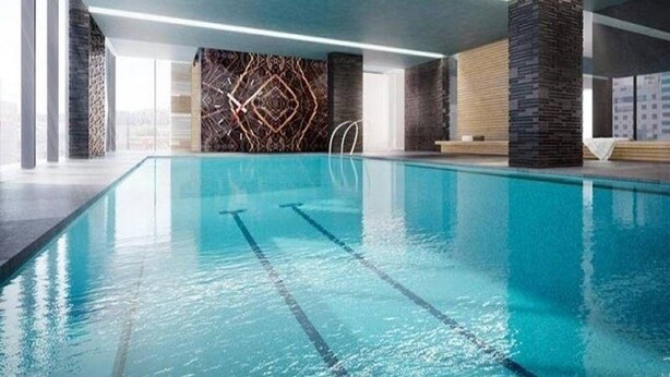 An indoor swimming pool with clear lane markings, a modern design with a geometric wall pattern, and a stone pillar on one side.
