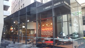 A restaurant with a glass facade, outdoor seating, and a neon sign.