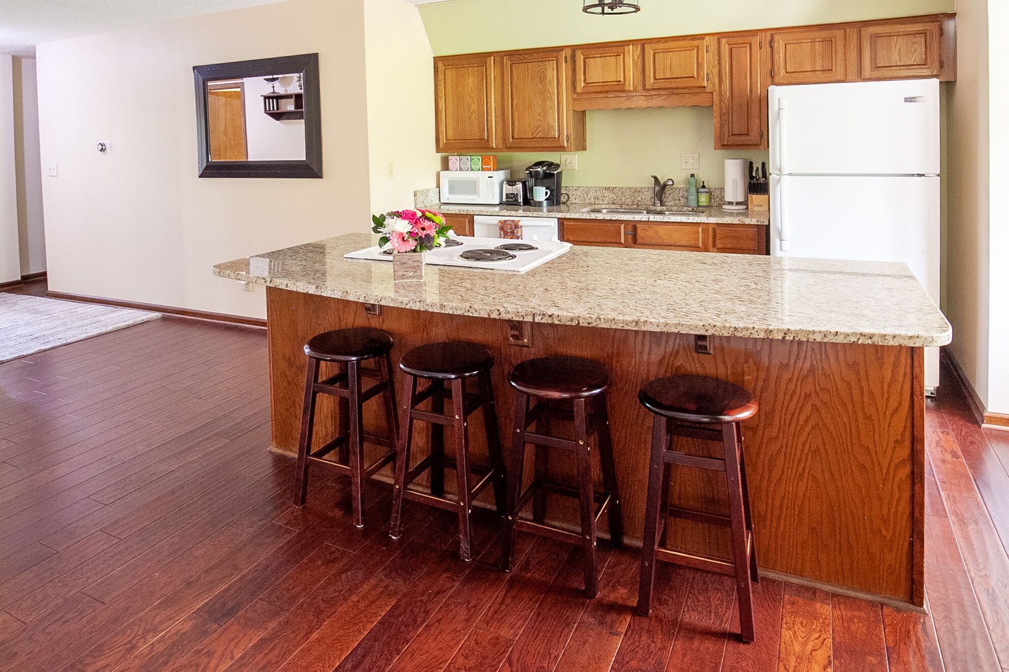 A kitchen with wooden cabinets, a white refrigerator, a granite countertop, and a bar stool area.