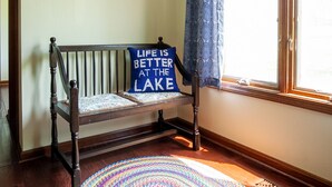 A room with a wooden bench, a colorful woven rug, a framed picture on the wall, and a window with a curtain. - Rock Creek Loft Guest House neighboring Lake Perry  (Ozawkie)