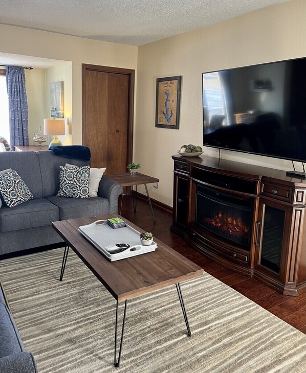 Una sala de estar con sofá, mesa de centro, televisor de pantalla plana y chimenea.