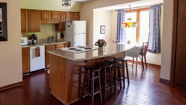 A kitchen with wooden cabinets, a white refrigerator, a granite countertop, and a bar stool area. - Rock Creek Loft Guest House neighboring Lake Perry  (Ozawkie)