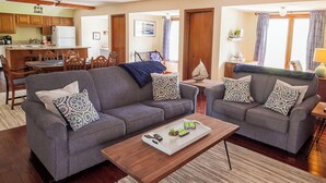 A living room with two grey sofas, a wooden coffee table, and a kitchen in the background. - Rock Creek Loft Guest House neighboring Lake Perry  (Ozawkie)
