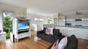 A modern living room with a flat-screen TV, a dark grey sofa, and a white entertainment unit. - Seascape  1 - Water views (BERMAGUI)