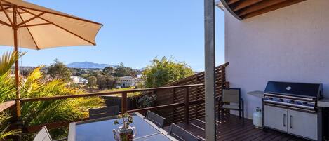 Une terrasse avec une table, des chaises, un barbecue et une vue sur la ville et les montagnes.