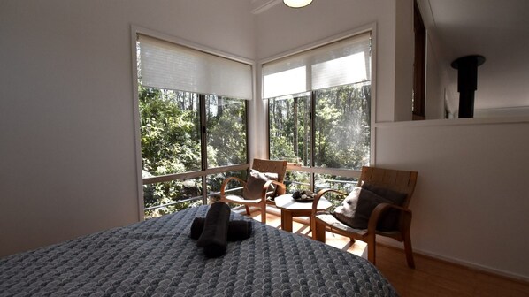 A room with a bed, two chairs, a window with a view of trees, and a ceiling light. - 11 Burrawong Place - Bushland Haven (BARRAGGA BAY)