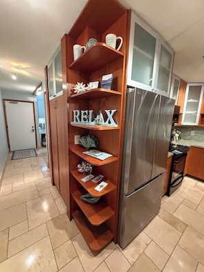 Una cucina con frigorifero integrato, mensole in legno con oggetti decorativi e un cartello con la scritta 'RELAX'.