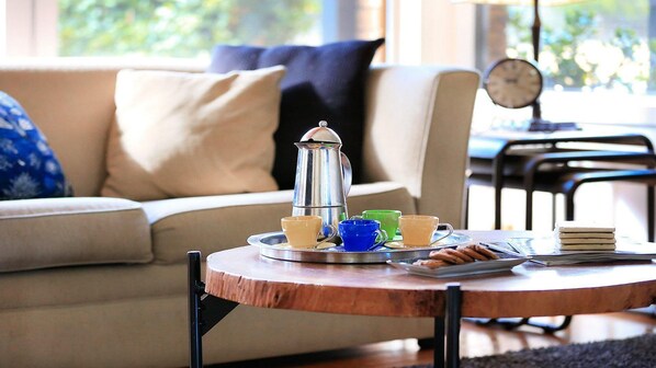 Una sala de estar acogedora con una mesa redonda de madera, un sofá color beige y un cojín azul estampada.