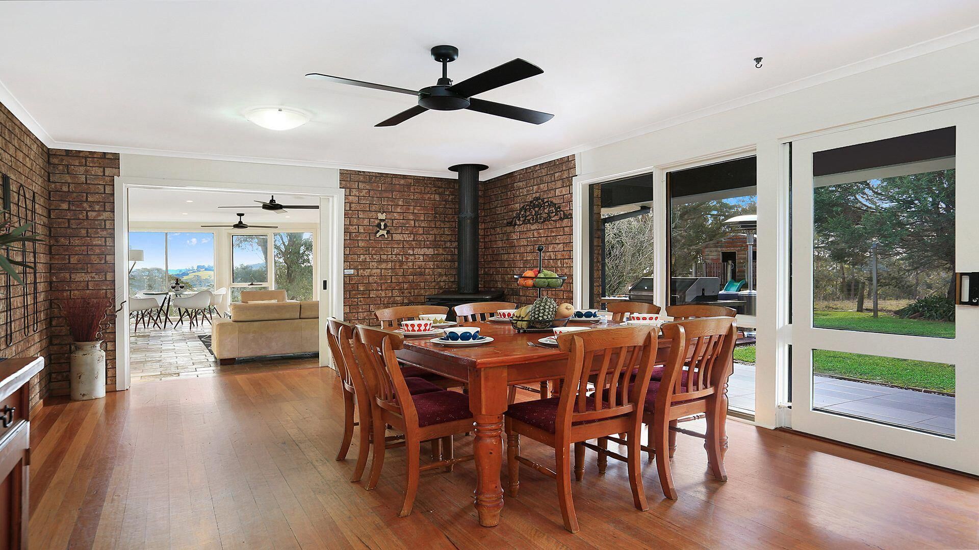 A dining area with a wooden table and chairs, a brick wall, and a view of the outdoors.