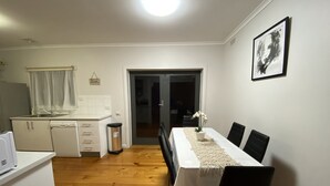 A compact kitchen with a dishwasher, a trash bin, and a dining area with a table and chairs.