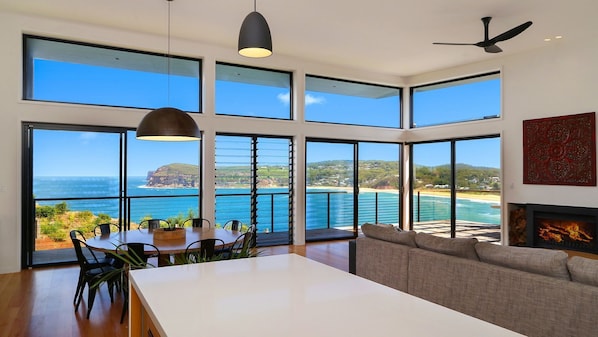 Un interior moderno con comedor, sofá y chimenea, con vistas a la costa.