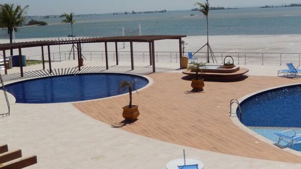 Un espace piscine comprenant deux piscines, un coin salon couvert et une vue sur la plage.