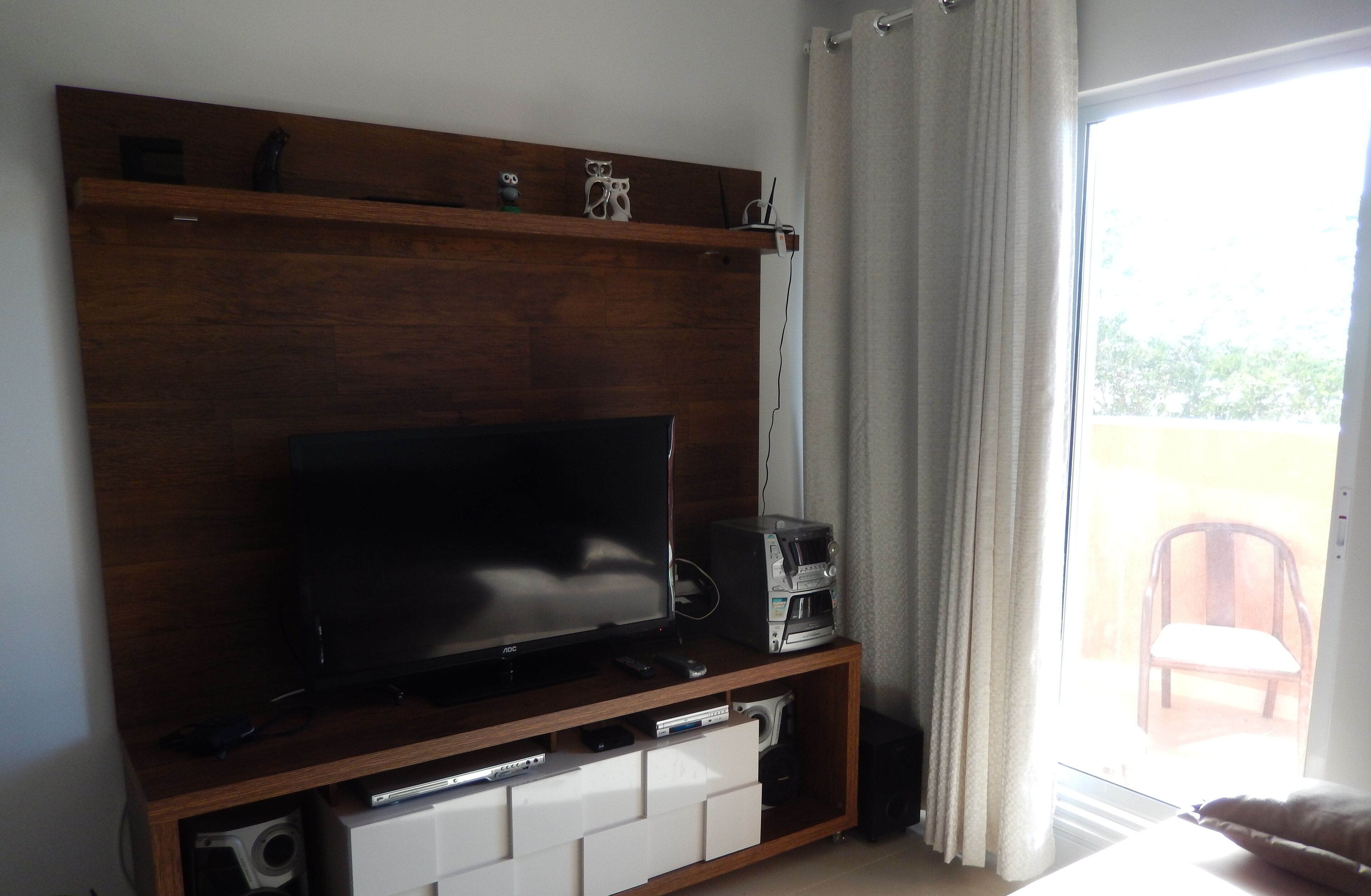 Una sala de estar con un televisor de pantalla plana sobre un soporte de madera, una cafetera y un ventanal corredizo que da a un área exterior.
