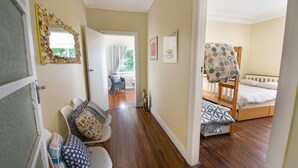 Une chambre avec un lit superposé, une chaise avec des coussins à motifs, un miroir avec un cadre en forme de coquillage et une porte donnant sur une autre pièce.