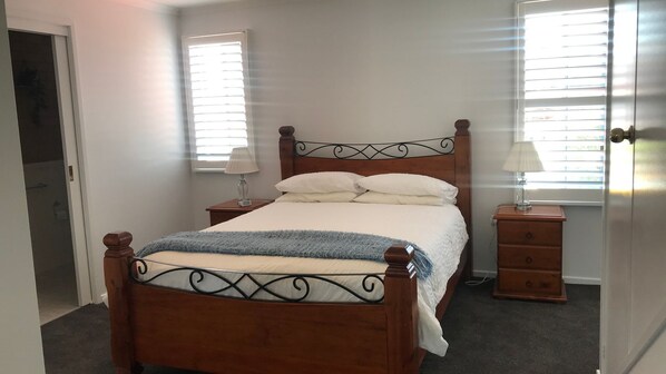 Un dormitorio con una cama de madera, dos mesitas de noche y un ventanal con persianas.