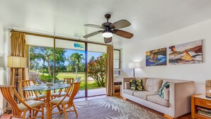 Ein Wohnzimmer mit Glastür zu einer Terrasse, Deckenventilator, Sofa, Couchtisch und zwei Gemälde.