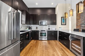 A modern kitchen with stainless steel appliances, dark cabinetry, and a wooden floor.