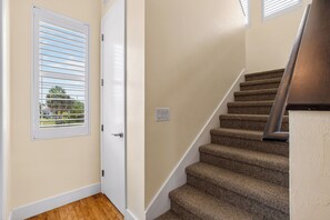 A staircase with carpeted steps leading to a landing, a white door with a window, and a light switch on the wall.