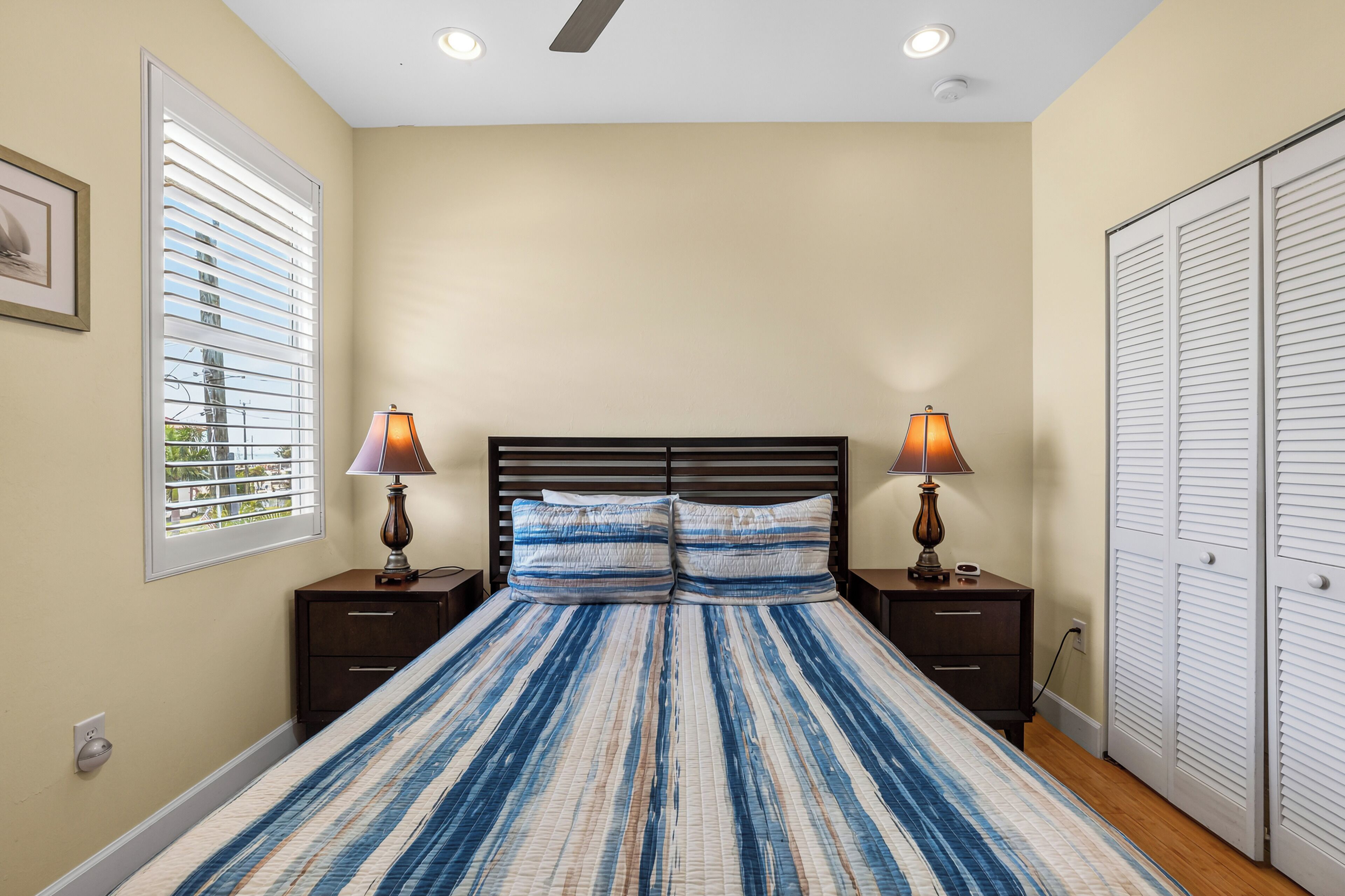 A bedroom with a bed, two nightstands, a window with blinds, and a closet.