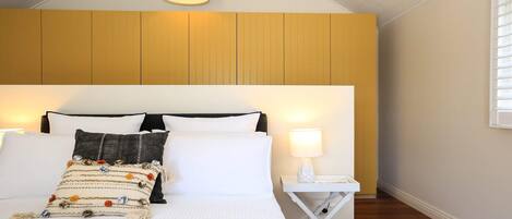 Une chambre à coucher avec un grand lit, une table de chevet avec une lampe et une fenêtre avec des stores.
