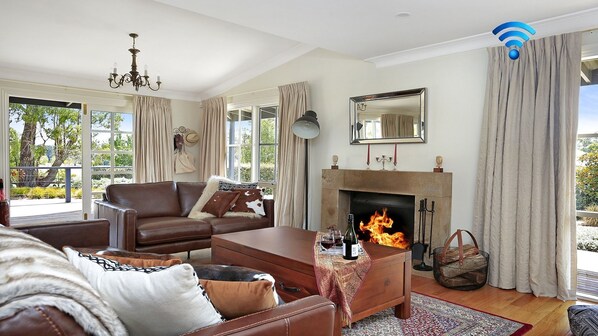 Amplia sala de estar con chimenea, mobiliario de cuero y grandes ventanales que ofrecen vistas al exterior.