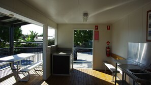 Un petit espace de cuisine extérieur, à l’abri, comprenant un banc, un évier et un extincteur.